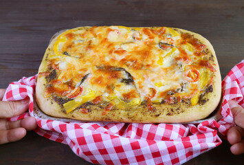 Man's hand placing delectable fresh baked homemade pesto veggie pizza on the table