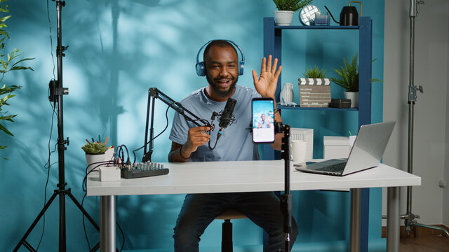 African american vlogger using smartphone to film podcast in studio. Black blogger with mobile phone, microphone and headphones filming video for social media broadcasting career.