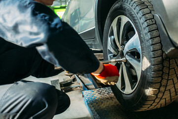 car service, the car is on a lift, the worker removes / installs the wheel, he has a tool in his hands