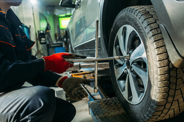 car service, the car is on a lift, the worker removes / installs the wheel, he has a tool in his hands