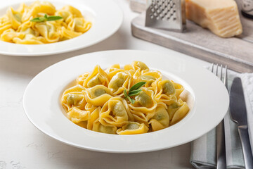 Plates with tortelloni stuffed with spinach and ricotta, stir-fried with melted butter and sage leaves. Parmesan cheese. White background.