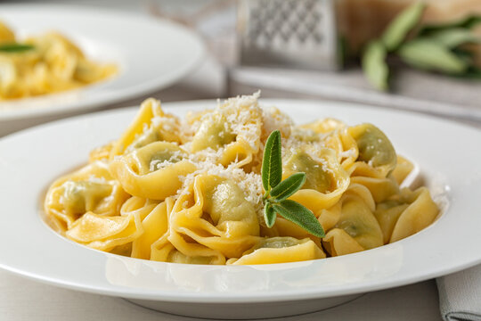 Close-up of tortelloni stuffed with spinach and ricotta, stir-fried with melted butter and sage leaves. Grated parmesan cheese.