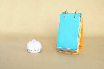 White timer and table flip calendar with a blank bright blue sheet on empty beige background....