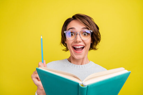 Photo of impressed young brunette lady read book wear eyeweear blue sweater isolated on yellow color background