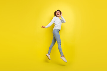 Fototapeta na wymiar Photo of crazy shocked funny lady jump look empty space wear blue sweater jeans footwear isolated yellow color background