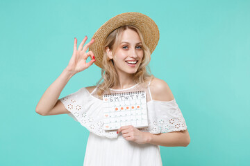 Smiling young woman in white dress hat hold female periods calendar for checking menstruation days isolated on blue turquoise background. Medical healthcare gynecological concept. Showing OK gesture.