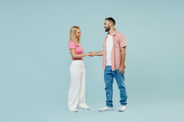 Full body side view happy young couple two friends family man woman in casual clothes hold hands folded handshake gesture together isolated on pastel plain light blue color background studio portrait.
