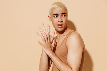 Side view young worried wondered tender blond latin hispanic gay man with make up in beige tank...
