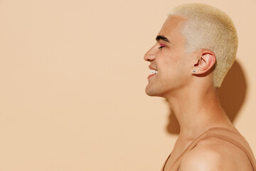 Side view young attractive smiling blond twink latin gay man 20s with make up closed eyes in beige...