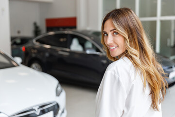 Fototapeta na wymiar Happy smiling fun woman 20s customer female buyer client in white shirt choose auto want to buy new automobile walk go in car showroom vehicle salon dealership store motor show indoor. Sales concept.