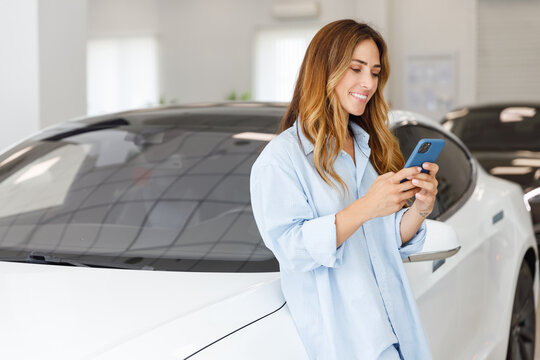 Happy woman customer female buyer client wears blue shirt use mobile cell phone choose auto want to buy new automobile in car showroom vehicle salon dealership store motor show indoor. Sales concept.