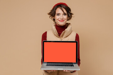 Naklejka premium Young smiling happy cheerful woman 20s wears red turtleneck vest beret hold use work on laptop pc computer with blank screen workspace area isolated on plain pastel beige background studio portrait