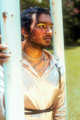 dreamy portrait of a dark skinned Indian man in Malaysia, with make up, in a field, surrounded by...