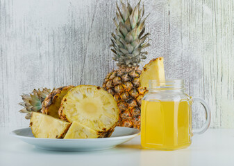 Fototapeta na wymiar Pineapples with juice in a plate on white and grungy background, side view.