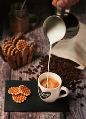 Person pouring milk in cup with coffee