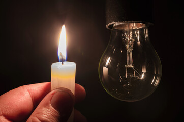 Burning candle near a switched off light bulb. Blackout, electricity off, energy crisis or power...