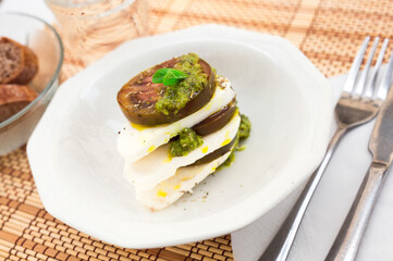 caprese salad with mozzarella, black tomatoes and pesto in white plate