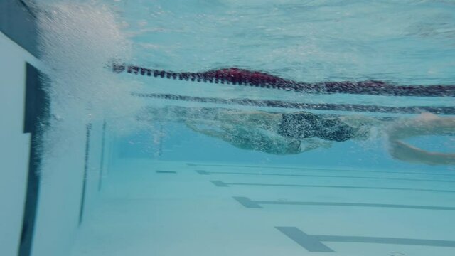 Underwater shot of a swimmers using tumble turn to reverse direction in the pool, during freestyle swimming training.