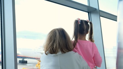 happy Mother and little girl at the airport in anticipation of landing look out the glass window at...