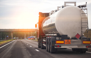 A truck with a tank trailer transports a liquid dangerous cargo on a highway against the backdrop...