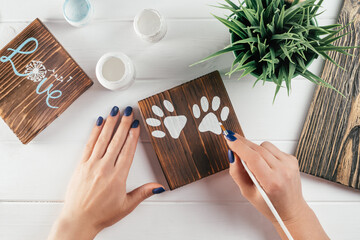 Womans hand draws paw prints on decorative board made of burnt wood with brush of white paint, creative DIY