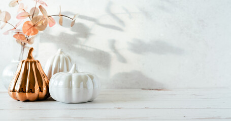 Fototapeta premium Details of Still life, pumpkins, candle, brunch with leaves on white table background, home decor in a cozy house. Autumn weekend concept. Fallen leaves and home decoration