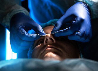 Doctor plastic surgeon conducts an operation of a female patient to reduce the shape of the nose,...