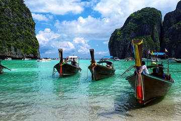 Longtale boats at the Phuket beach with rocks on background in Thailand. Phuket island is a most popular tourist destination in Thailand.