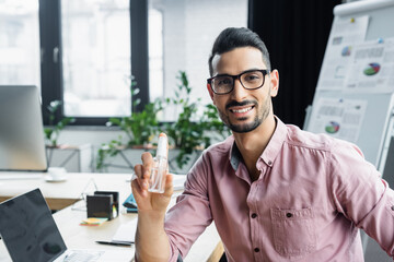 Smiling muslim businessman holding hand sanitizer in office