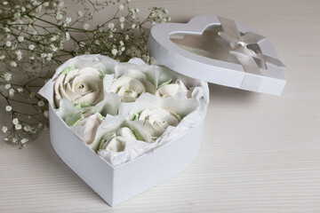 Homemade marshmallow in a gift box. Zephyr roses.  Heart shaped box. Tied with a ribbon tied to a bow. Marshmallow roses.  Heart shaped box.  Nearby is a bouquet of gypsophila.