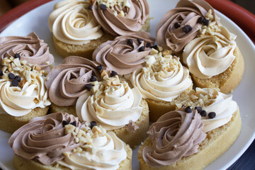 Sponge cake decorated with cream and chocolate drops.  Are laid out on a platter.  They stand on a surface made of pine boards.  Close-up shot.