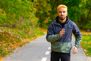 Fototapeta na wymiar Running man with copy space. Man with dyed hair in blonde jogging in the autumn park.