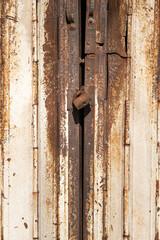 Rustic metal gate which is closed with key padlock. Building material background and textured photo. Selective focus at the padlock part.