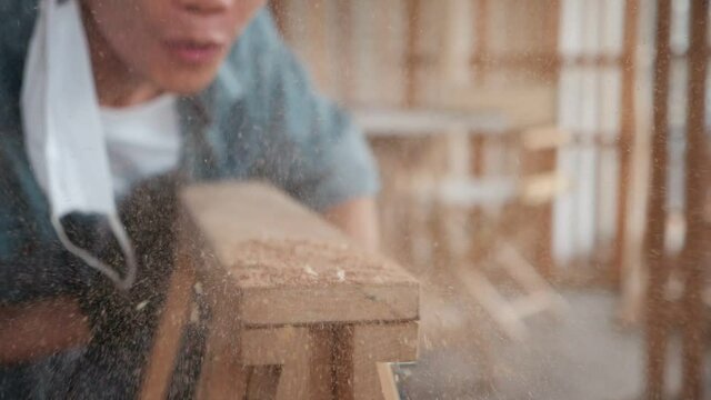 Carpenter working on wood craft at working to produce construction material or wooden furniture, blow dust on wood board. DIY maker and carpentry work concept.