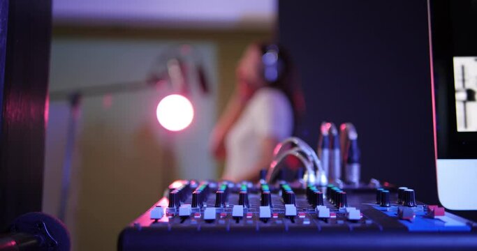 Close up of sliders and buttons on sound audio mixing desk with blurred of recording female voice in studio background