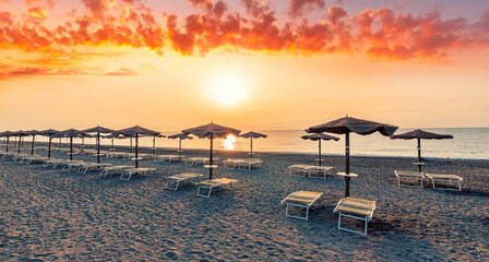 scenic view at nice sunset or sunrise beach with rows of umbrellas and chaise lounges with blue sea...