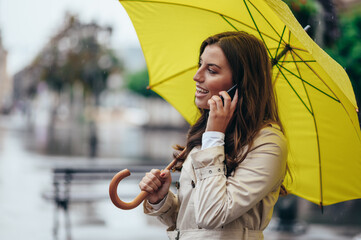 Woman using a smartphone and holding a yellow umbrella while out in the city