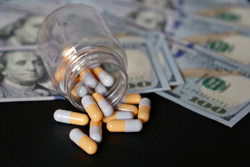 Pills in a bottle on US dollars bills on black table. Concept of health care in USA, pharmaceutical business, drug prices, pharmacy, medicine and economics