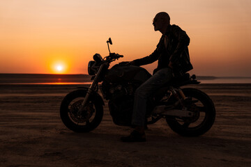 Fototapeta na wymiar Bold senior man wearing leather jacket posing on motorcycle outdoors