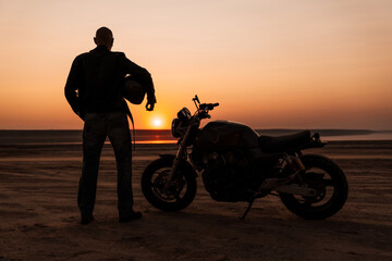 Bold senior man wearing leather jacket posing with motorcycle outdoors