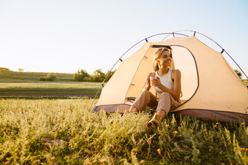 White woman drinking tea while sitting in tent during camping