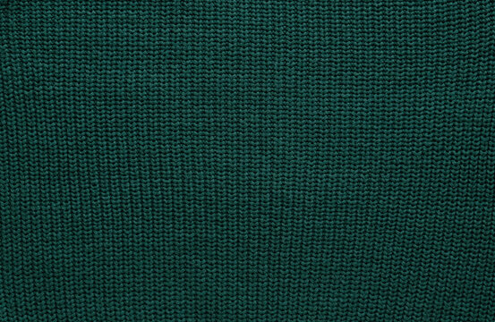 Texture of smooth knitted dark green sweater with pattern. Top view, close-up. Handmade knitting wool or cotton fabric texture. Background of Large Ribs knit pattern with knitting needles or crochet.
