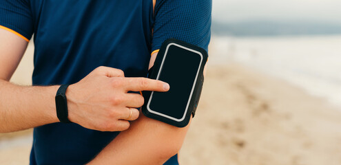 Sporty man is using his phone from arm band.