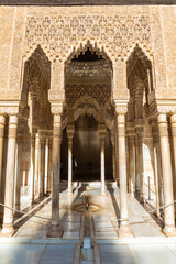 Arches and columns decorated with arabesques in the famous Palacio Nazaries (meaning: Nazaries Palace) in the Alhambra, Granada, Spain. Fountain with water on the ground.
