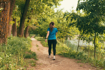 Active young woman is walking on a path in the forest on daytime. - Powered by Adobe