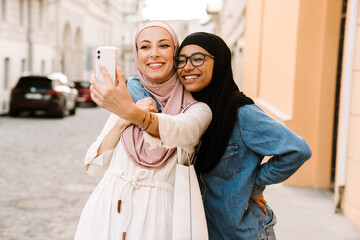 Multiracial muslim women wearing hijab smiling while using mobile phone