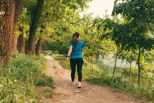 Active young woman is walking on a path in the forest on daytime.
