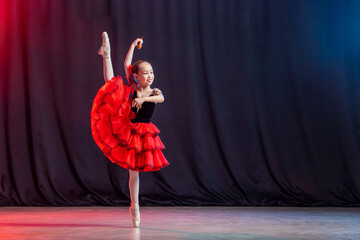 A little girl ballerina is dancing on stage in a tutu on pointe shoes with castanedas, the classic...