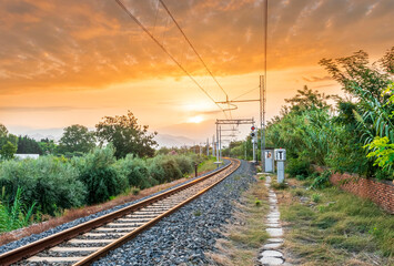 Fototapeta na wymiar old evening railroad leading to a sunset glow in mountains with green bushes and cjlorful cloudy sku on the background