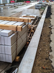 A stack of concrete new curbs prepared to replace the old canvas. Repair of the roadway and pedestrian zone. Everything is dug up, the process of construction work